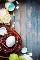 White egg in little nest with light flowers on wooden rustic background. Easter spring concept