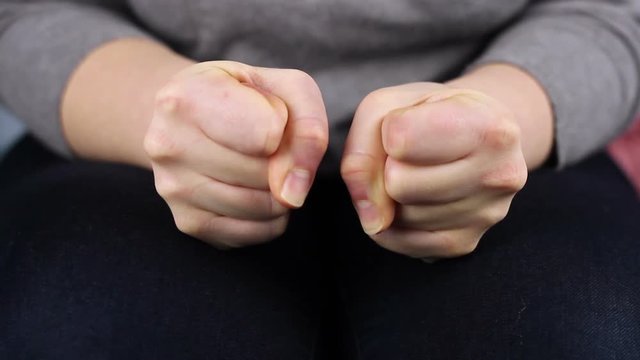 Close-up women's hands clench their fists.