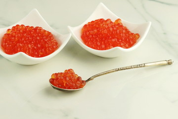 red caviar in white plates and in a spoon on a marble table. Copy space