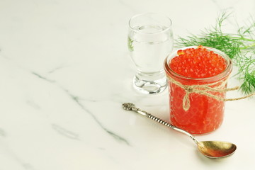 red caviar in a glass jar with a spoon on a marble table. Copy space