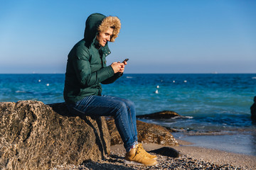 Smiling guy using his smartphone on the beach.