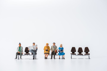 row of miniature people figure sitting on bench white background
