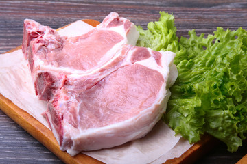 Raw pork steak with spices Leaves lettuce on wooden cutting board. Ready for cooking.