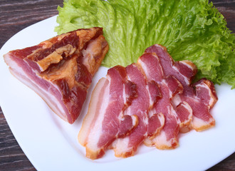 Fresh homemade smoked bacon with leaves lettuce on white plate. Selective focus.