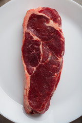 Raw beef marbled steak on a white plate. Steak New York. Top view close-up