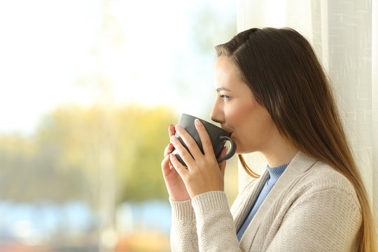 Lady drinking coffee and looking through a window