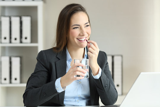 Happy businesswoman taking a pill at office