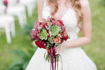 Stunning red bridal bouquet on white chair. Wedding ceremony. Mix of succulents, orchids and roses