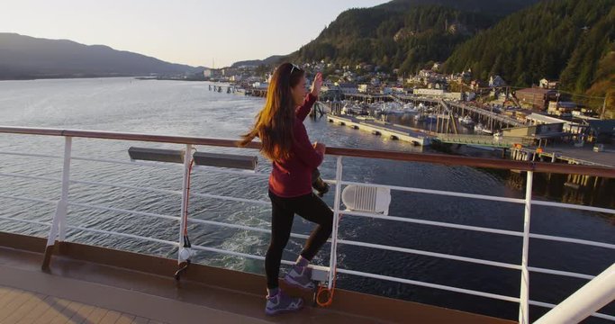 Alaska Cruise ship passenger in city of Ketchikan standing on cruise ship deck waving ashore while sailing away from Ketchikan in Inside Passage, a famous Alaska cruise ship destination.