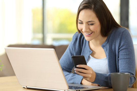Woman using a phone and laptop sitting at home