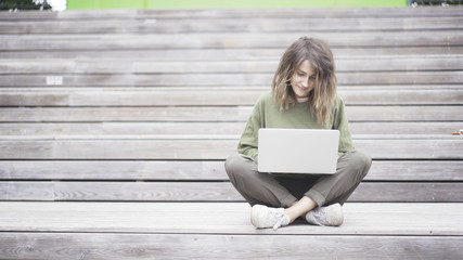 Woman sitting on the bench while typing on laptop. Wooden background. Front view.