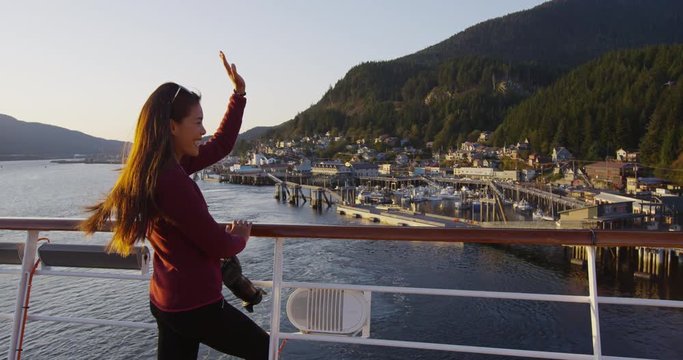 Cruise ship passenger in Alaska city of Ketchikan standing on cruise ship deck waving ashore while sailing away from Ketchikan in Inside Passage, a famous Alaska cruise ship travel destination.