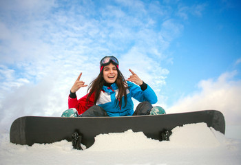 Joyful woman snowboarder sitting on top of mountain on blue sky