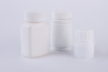 Three blank plastic bottles for medicine. White blank small and medium sizes plastic packaging bottles with cap for vitamins, grey background.