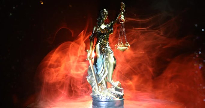 The statue of justice - lady justice or justitia goddess of Justice rotating on foggy fire orange background with light. Law concept with Themis symbol of justice