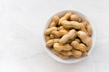 Pile of peanuts in ceramic bowl on concrete background with copy space. Top view.