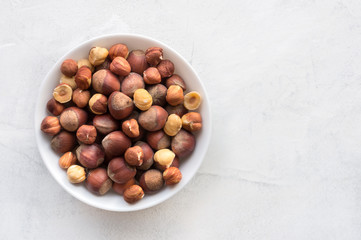 Pile of hazelnuts in ceramic bowl on concrete background with copy space. Top view.