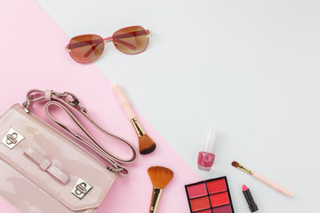 Table top view accessory of clothing women  plan to travel in holiday background concept.Hand bag with many essential  items cosmetic and sun glasses on modern white & pink paper.Duo with pastel tone.