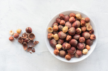 Pile of hazelnuts in ceramic bowl on concrete background. Top view.