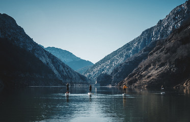 People paddle surfing on a lake in a snowy mountain landscape