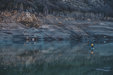 a woman with yellow plumber paddle surfing on a lake in a snowy mountain landscape