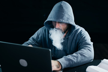 mysterious criminal man hides his face under the hood and smokes a hookah