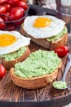 Making open sandwiches with mashed avocado and fried egg on bread, vertical