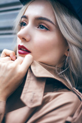 A young beautiful blonde woman is walking and enjoying small urban street in Shanghai. She is wearing nice long brown coat and black hat. Her gorgeous face is accentuated by a dark red lipstick.
