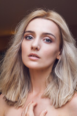 Close-up portrait of a gorgeous young blonde woman with straight cut hairstyle, green mysterious eyes looking at you through the lens, big sexy lips and completely unveiled.