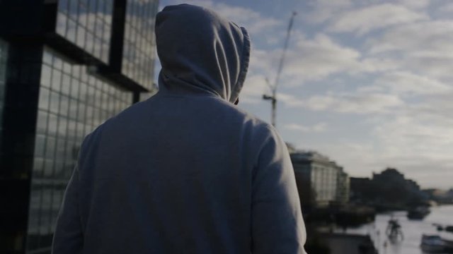 Hooded male jogger soaks in the view of the city in the morning sun, in slow motion