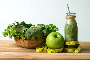 the Healthy fresh  green smoothie juice in the glass bottle on wooden table with green apple and  vegetables basket for healthy detox and diet  habits concept 