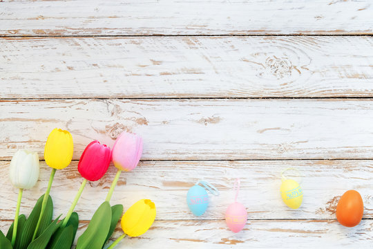 Colorful Easter eggs with tulip flower on rustic wooden planks background. Holiday in spring season. vintage pastel color tone. top view composition.