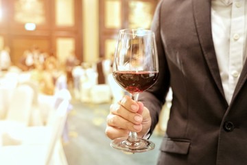 Close of of business man wearing suit holding a glass of wine in the company party with ray yellow light in the background. Concept and idea of business success, celebration party.