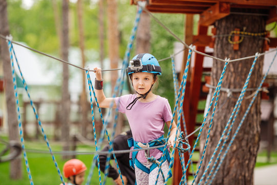 baby girl with climbing gear  in an adventure park are engaged in rock climbing or pass obstacles on the rope road.