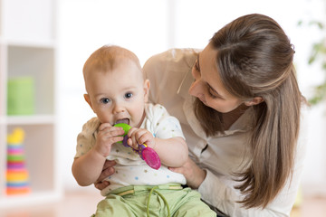 Baby sitting on mom knees bites toy © Oksana Kuzmina