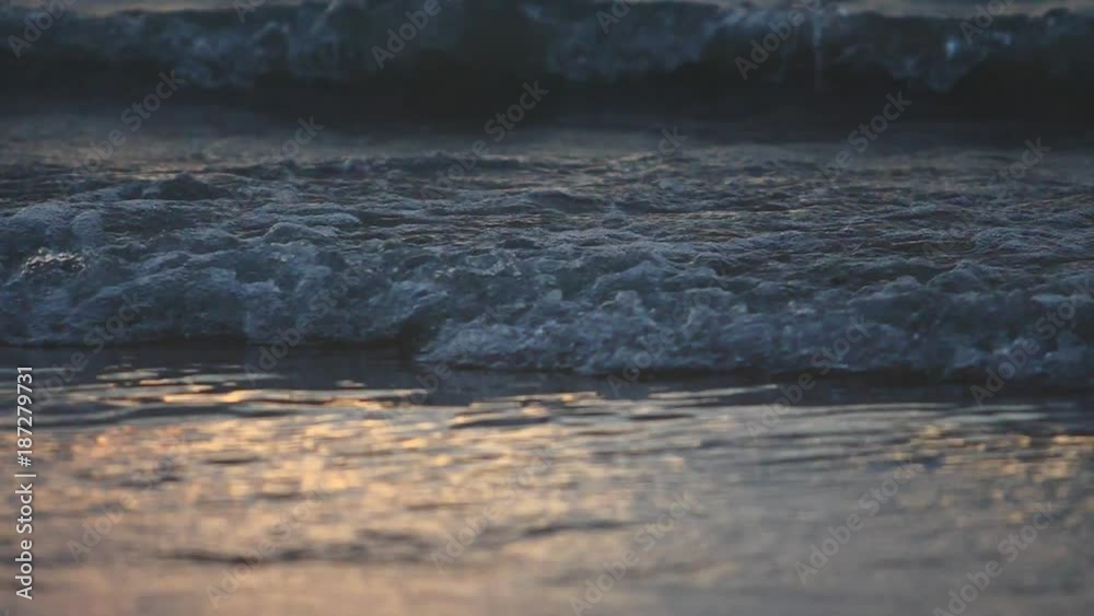Wall mural sea shallow water incoming waves with foam and splashes in slow motion on sunset background