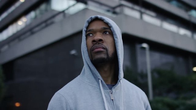 Camera circles a hooded jogger as he surveys the city around him, in slow motion