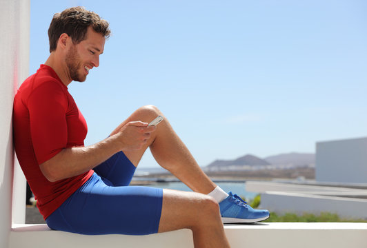 Fitness Sport Man Using Mobile Phone App After Workout Training Relaxing Sitting At Home Balcony. Technology And Sports Athlete Holding Smartphone. Active And Healthy Lifestyle.