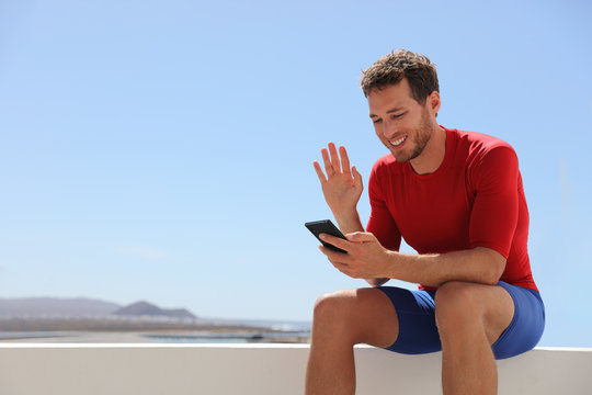 Man calling via video call on phone talking to someone waving hello during videochat conversation. Fit athlete personal trainer online at fitness gym.