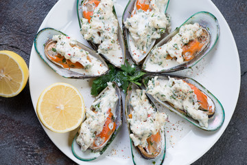 Above view of baked kiwi mussels with cheese sauce and lemon on a white plate, closeup