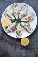 White plate with green mussels baked in cheese sauce, top view over grey stone background, vertical shot with space