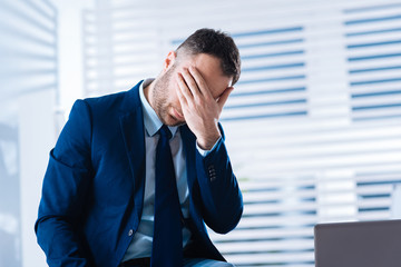 Oh no. Emotional hardworking businessman sitting in his office and feeling upset when closing his eyes after facing a misfortune at work