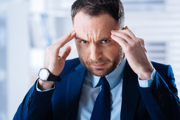 Intensive thinking. Serious smart bearded businessman in a dark blue suit looking concentrated while thinking and touching his head