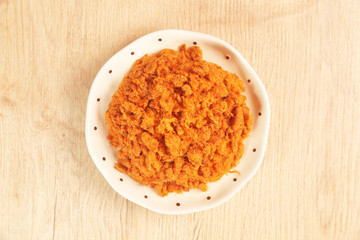 Dried shredded pork in a plate on wooden table.