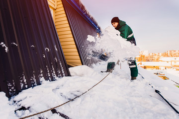 Snow cleaning. Team of male workers clean roof of building from snow with shovels in securing belts of mantra.