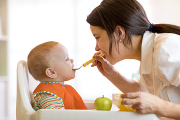 Mom giving fruit puree to her baby son on high chair.
