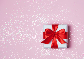 gift box vith red bow and glitter sparkles on pink background. st. Valentine's day concept