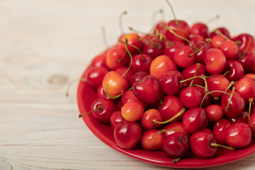 Cherries on a red plate on a light wooden background.
