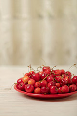Cherries on a red plate on a light wooden background.