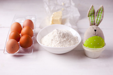 Fototapeta na wymiar Ingredients for cooking dough, sweet baking. Bowl of flour, butter, eggs, baking molds and toy bunny, Easter spring background